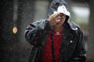 A man pulls his raincoat over his head as he walks in the rain in Beijing, Wednesday, July 20, 2016. A strong weather system brought heavy rain to China's capital on Wednesday