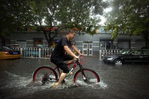 A bicyclist rides down a flooded side street in the rain in Beijing, Wednesday, July 20, 2016.