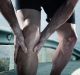 young sport man with strong athletic legs holding knee with his hands in pain after suffering muscle injury during a ...