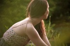 Young Woman Sitting In Field At Sunset