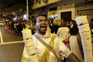 Cyrus Oliveira yells as he runs with torches for sale while others wait to see the Olympic torch in the streets of Copacabana on its journey to the opening ceremony of the 2016 Summer Olympics in Rio de Janeiro, Brazil, early Friday, Aug. 5, 2016.