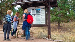 Three hikers standing in front of a trailhead sign