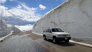 An SUV on the road beside a 15 foot tall snow drift