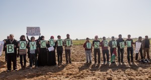 Palestinian and international activists hold signs in support of the Boycott, Divestment and Sanctions (BDS) movement by the buffer zone in Zeitoun on 9 February 2013.