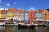 Historical wooden ships anchored before colourful townhouses in Nyhavn, Copenhagen, Denmark.