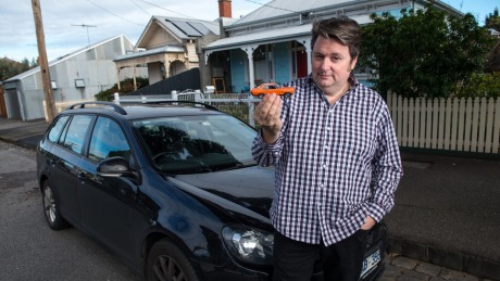 Comedian Dave O'Neil poses for a photo with his VW Golf TSI while holding a model of his first car (Holden Torana).