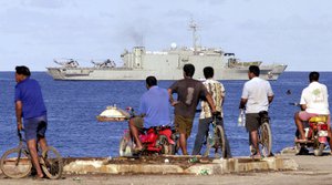 File - Local men watch as the Australian navy ship HMAS Manoora moves slowly along the Nauru coast Tuesday, Sept. 18, 2001. The Manoora, carrying hundreds of refugees picked up in Australian waters weeks ago, loomed close to Nauru's shores Tuesday, as it prepared to offload its human cargo onto this tiny Pacific island state.