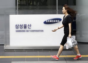 An office worker walks by a logo of Samsung C&T Corp., at its head office in Seoul, South Korea, Friday, July 17, 2015. Samsung shareholders approved Friday a highly contested deal that strengthens the Samsung family’s grip on the world’s largest smartphone maker. Company Samsung C&T said that 69.5 percent of shareholders who voted supported the takeover of it by another Samsung company, Cheil Industries.(AP Photo/Ahn Young-joon)