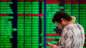 A man uses his mobile phone in front of electronic stock boards at the Australian Securities Exchange (ASX Ltd.) ...