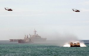 A US Navy (USN) Landing Craft-Air Cushion (LCAC) craft, approached the beach at Samesan Royal Thai Marine Base, Thailand, as two US Marine Corps (USMC) CH-53E Sea Stallion helicopters assigned to Marine Heavy Helicopter Squadron 462 (HMH-462) fly over head. In the background the US Navy (USN) WHIDBEY ISLAND CLASS: Dock Landing Ship, USS FORT McHENRY (LSD 43) and an unidentified utility craft lie off shore. All part of an amphibious assault exercise conducted during Exercise COBRA GOLD 2002.