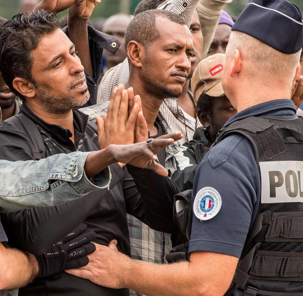 Migrants from the 'Jungle' migrant camp wait under police surveillance for a bus heading to a "Welcome and orientation centre" (CAO), on September 13, 2016 in Calais, as part of a plan to dismantle the camp. / AFP PHOTO / PHILIPPE HUGUEN