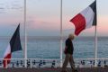 A man walks past French flags flying at half mast on the Promenade des Anglais in July.