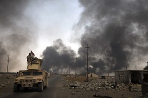 In this Wednesday Aug. 31, 2016 photo, Iraqi security forces patrol as smoke rises from burning oil wells in Qayara, Iraq.