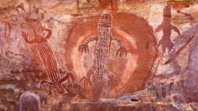 Indigenous rock art showing red animal figures on brown rock.