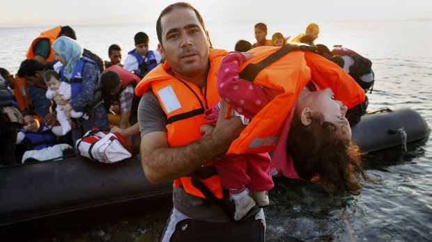 A Syrian refugee carries a child as they arrive at a beach on the Greek island of Kos after crossing the Aegean Sea from ...