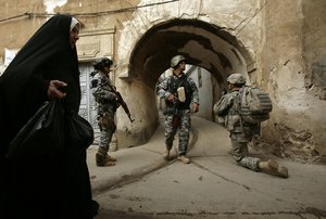 In this Thursday, April 23, 2009 file photo, an Iraqi woman passes U.S. troops and Iraqi police officers as they stand guard in the Bab al-Jadeed area of Mosul, Iraq. Iraq's security forces are converging on the city of Mosul, lining up for a battle on the historic plains of northern Iraq that is likely to be decisive in the war against the Islamic State group.