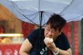 A woman, Mrs Dai, eats a pork bun while struggling with her umbrella against the powerful generated by typhoon Megi in ...