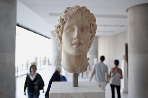 Visitors walk behind an ancient marble head of ancient Greek warrior-king Alexander the Great, displayed at the Acropolis museum in Athens, Oct. 12, 2014.