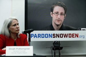 File - Dinah PoKempner, left, general council for Human Rights Watch, listens as Edward Snowden speaks on a television screen via video link from Moscow during a news conference to call upon President Barack Obama to pardon Snowden before he leaves office, Wednesday, Sept. 14, 2016, in New York.