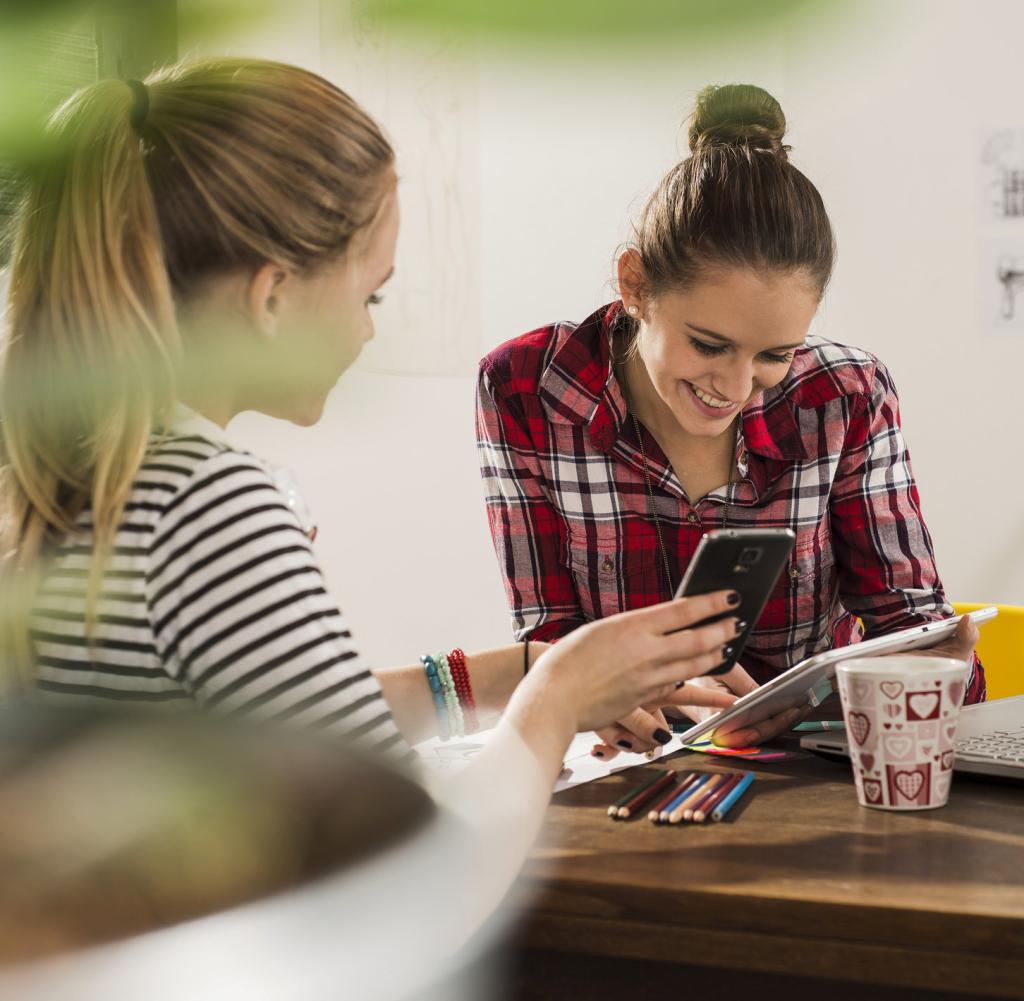 Two female friends with smartphone, laptop and digital tablet at home