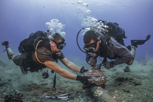 Chief Construction Electrician Daniel Luberto, right, and Construction Mechanic 3rd Class Andersen Gardner, assigned to Underwater Construction Team 2, Construction Dive Detachment Bravo (UCT2 CDDB), remove corroded zinc anodes from an undersea cable at the Pacific Missile Range Facility Barking Sands, Hawaii