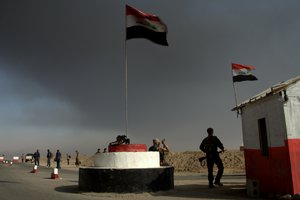 Iraqi troops guard a checkpoint near the village of Awsaja, Iraq, as smoke from fires lit by Islamic State militants at oil wells and a sulfur plant fills the air on Saturday, Oct. 22, 2016.