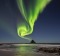 The green band of Auroras seem like smoke from the top of the rock.