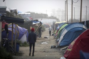 People walk along a street in a makeshift migrant camp near Calais, France, Sunday, Oct. 23, 2016.