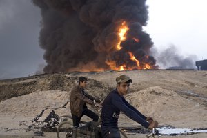 In this Sunday, Oct. 23, 2016 file photo, youths ride bicycles next to a burning oil well in Qayara, about 31 miles (50 km) south of Mosul, Iraq.