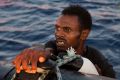 A migrant from Eritrea holds onto the side of a boat after jumping into the water from a crowded wooden boat during a ...