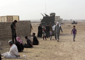 Civilians leave their houses as a member of Iraq's elite counterterrorism forces interrogates handcuffed suspects of Islamic State in the village of Tob Zawa, about 9 kilometers (5½ miles) from Mosul, Iraq, Tuesday, Oct. 25, 2016.