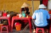 A woman selling Cau Lau, a local noodle specialty on a street sidewalk in Hoi An, Vietnam.