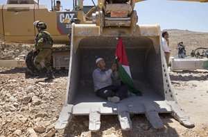 A Palestinian man tries to stop work by an Israeli bulldozer during a protest outside the village of Deir Qaddis, near the West Bank city of Ramallah, Wednesday, July 13, 2016.