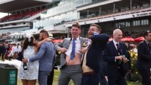 Woman leans on man (L), men in suits lift their shirts to show their stomachs (R) in spectator area 