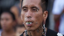 Man wears multiple piercings in eyebrows, nose, mouth, cheeks