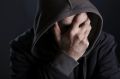 Depressed man looking despaired, hiding face with hand and hood, isolated on black background.