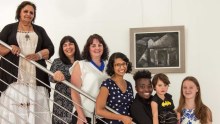 Seven women of different ages stand on a staircase.