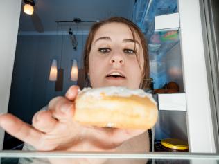 portrait of woman taking donut from fridge