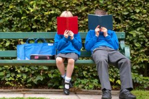 two children in school uniform reading books on a park bench