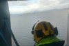 Searcher in helicopter door looking down over the sea.