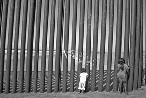 Tijuana view of the US-Mexico barrier steel border division fence, with children peering into California.