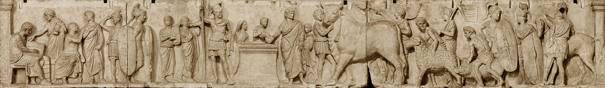 Relief depicts a long continuous scene that may be divided into three main groupings from left. The first is a group of four men wearing togas. Two are seated, and one is writing in a tablet. Two tall military guards divide this group from the central scene of sacrifice. Two musicians, markedly shorter than the soldiers, play a lyre and a horn. An unadorned altar, waist-high, stands in the center. To the viewer's left is the tallest figure in the composition, a military officer wearing a high plumed helmet and holding a long slender spear. standing by an altar. On the other side of the altar a priest, his head ritually covered, extends a libation bowl. A boy attendant pours from a pitcher into the bowl, and to that boy's right is a smaller boy looking on and lifting his right hand to the top of his head, a gesture that appears quizzical to modern viewers but may have some other significance in its Roman context. The priest is accompanied by a third boy close to his left side who stands ready with a towel. The right side of the relief is devoted to the procession of the three animal victims for the suovetaurilia, each led by a young male attendant, barechested but wearing a short kilt-like garment, with a wreath on his head. The first leads a enormous bull with a tasseled rope dangling from below its left horn. A fourth male attendant in the same attire follows closely on the bull's hindquarter, waving a palm branch in each hand. The attendant bringing the ram is followed by another veiled figure carrying a pole from which a banner unfurls. The attendant herding the pig is followed by another soldier bearing a long shield and looking back at another whose shield rests on the ground, covering most of his body. The last figure is a cavalryman, back turned to the viewer, next to his horse.