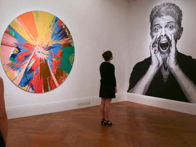 An artwork entitled 
<i>Beautiful, shattering, slashing, violent, pinky, hacking, sphincter painting</i> by British artist Damien Hirst next to a portrait of music legend David Bowie.