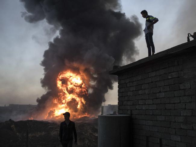 People watch as safety workers try to extinguish fire from a burning oil field in Qayara, south of Mosul, Iraq. Picture: AP