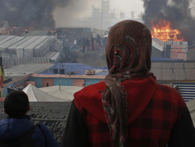 People stand on a hill as smoke and flames rise from amid the tents, after fires were started in the makeshift migrant camp known as &quot;the jungle&quot; near Calais, northern France. Picture: AP