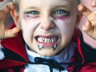 Portrait of a little boy dressed up as halloween vampire. The boy is aged 6 and is making scary face at the camera.