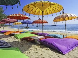 This image shows some colourful beach umbrellas and sand pillows in a pristine tropical beach bathed by the Bali sea.