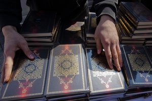 FILE - In this April 14, 2012 file photo a member of a Muslim group prepares copies of the Quran for distribution at Potsdamer Platz in Berlin. Hundreds of police officers searched about 190 offices, mosques and apartments of members and supporters of the Islamic group