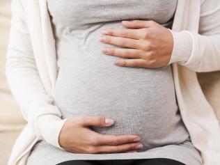 Close-up of young pregnant woman touching her abdomen while sitting on the couch