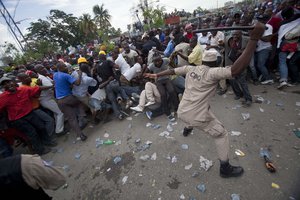 A police officer uses his baton to beat back supporters of Haiti's former President Jean-Bertrand Aristide who gathered outside the courthouse where Aristide arrived earlier in the day in Port-au-Prince, Haiti, Wednesday, May 8, 2013.